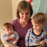 Mom finding contentment while sitting in a rocking chair with her infant and toddler on her lap reading before bedtime