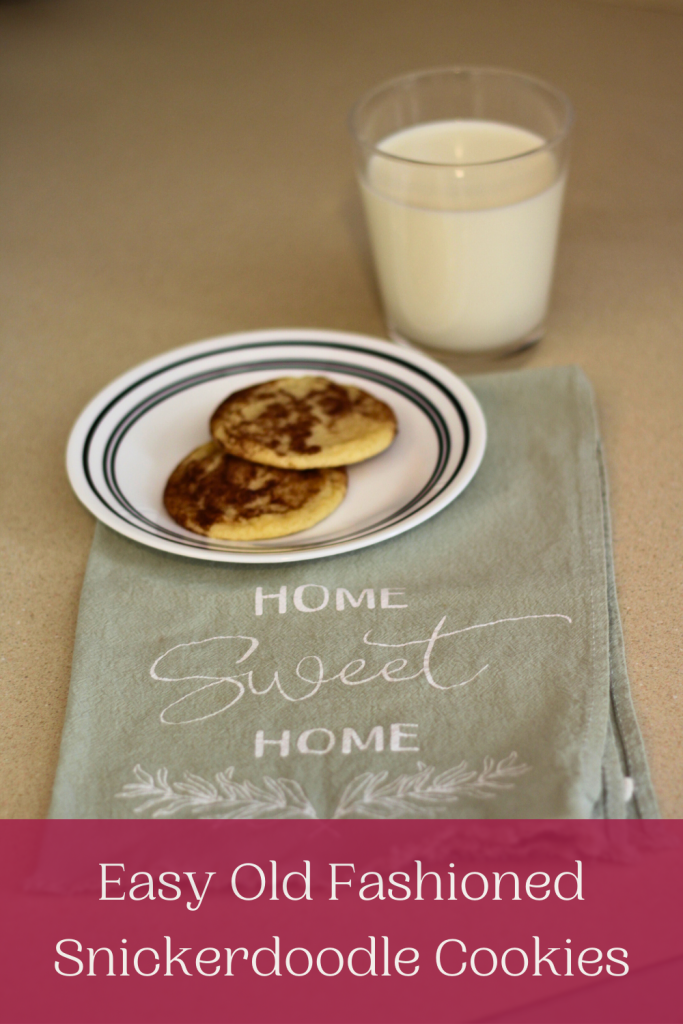 Image of 2 old fashioned snickerdoodle cookies on a plate set on a green towel that says 'Home Sweet Home' with a glass of milk in the background.