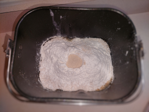 picture of ingredients in the bread machine bowl with flour well filled with the yeast